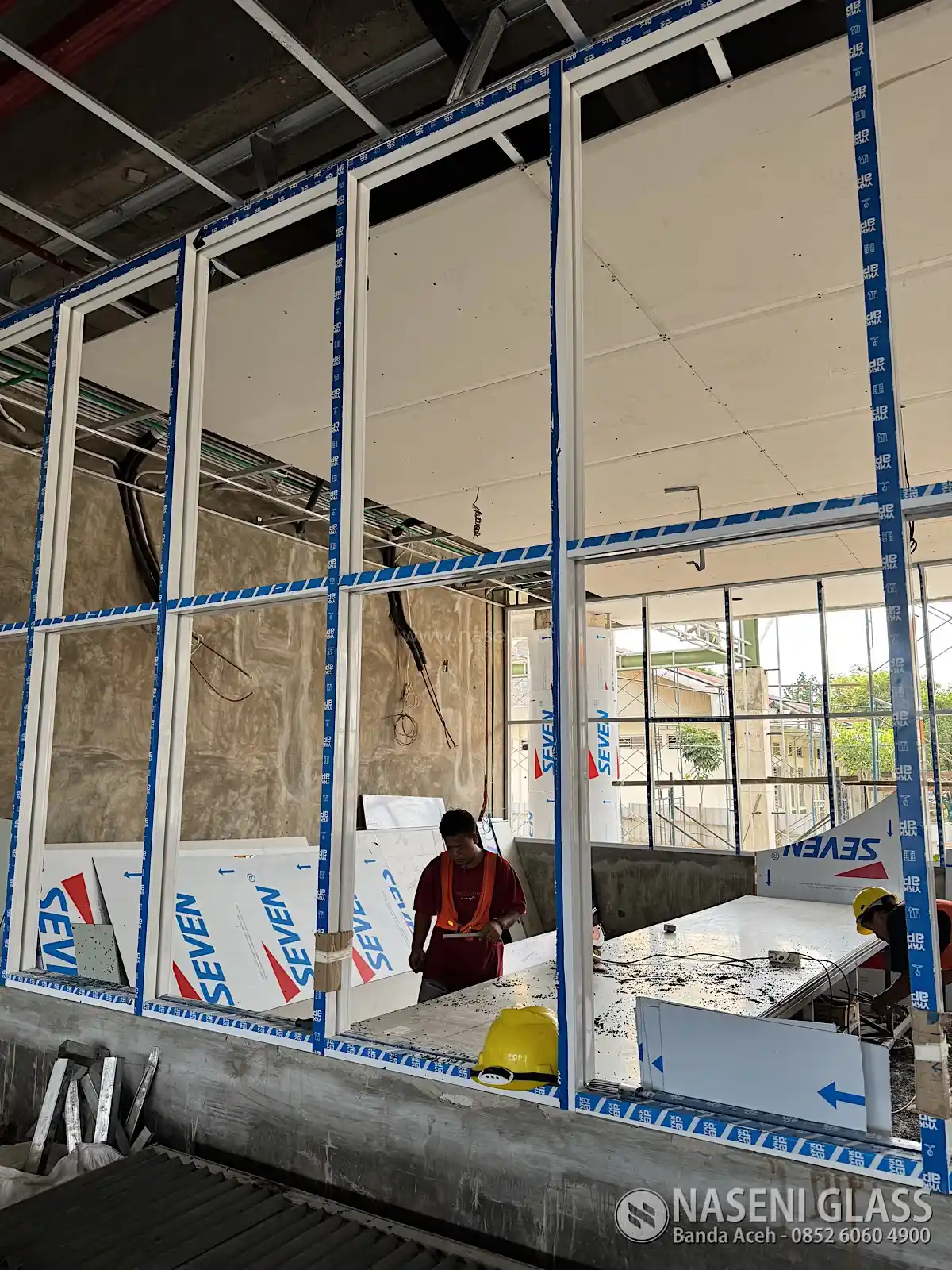 Proses pemasangan partisi aluminium YKK 4 inci pada interior Gedung TDC Politeknik Lhokseumawe.